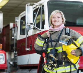 firefighter in gear smiling and standing in front of a firetruck